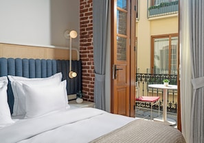 Une chambre d’hôtel comprenant un lit, une table de chevet, une lampe, une fenêtre avec des rideaux et donnant sur le balcon extérieur.