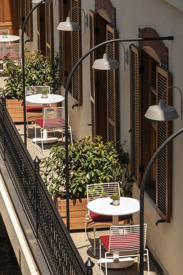 Un café en plein air avec des tables et des chaises, entouré de volets en bois et de plantes en pot.