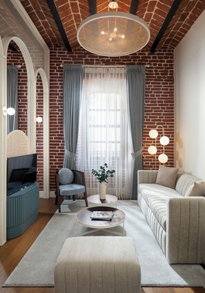 Una sala moderna con pared de ladrillo, una lámpara redonda en el techo, un sofá, un sillón, una mesa de centro y un televisor.