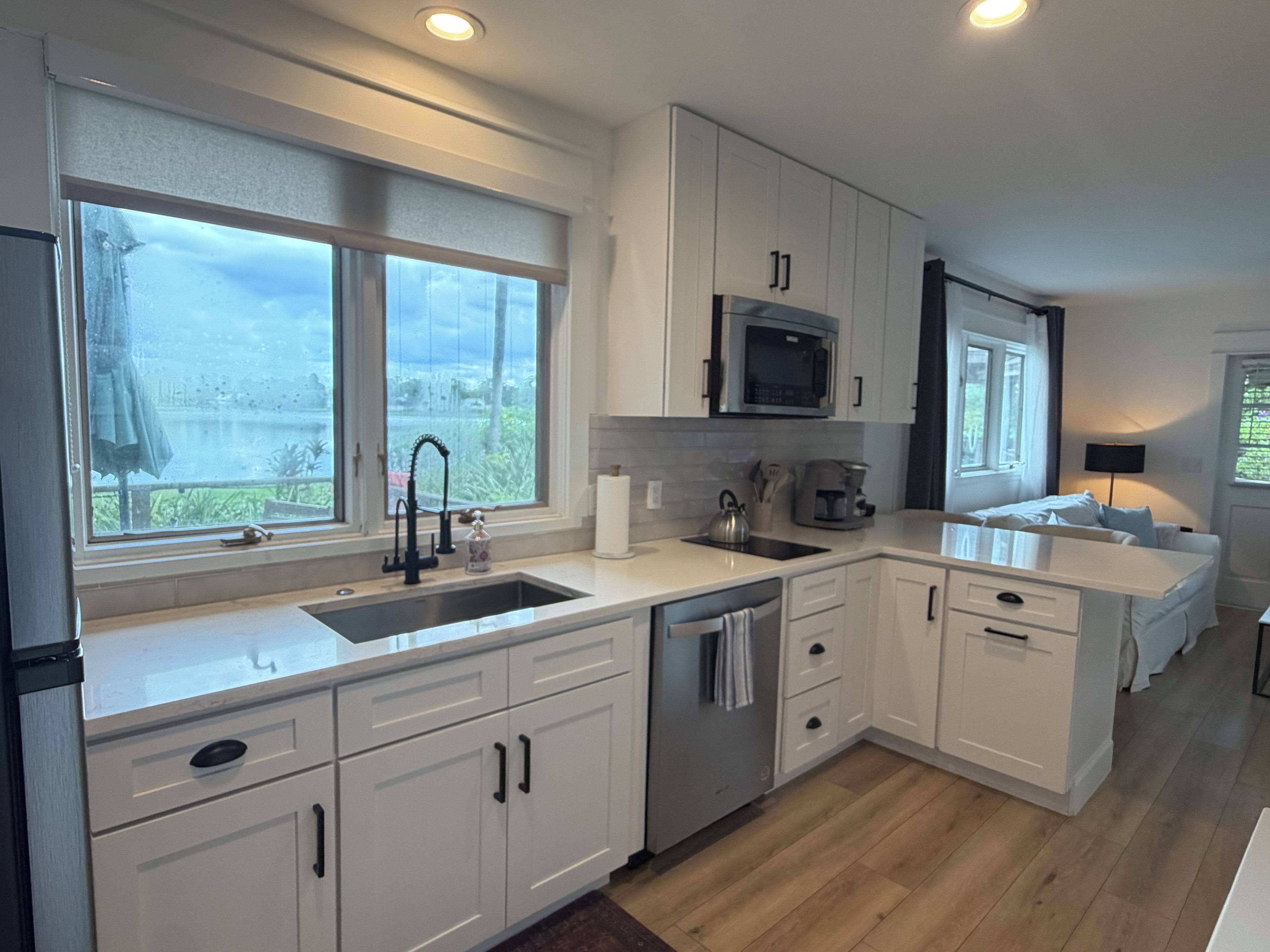 A modern kitchen with white cabinetry, a stainless steel sink, and a microwave.