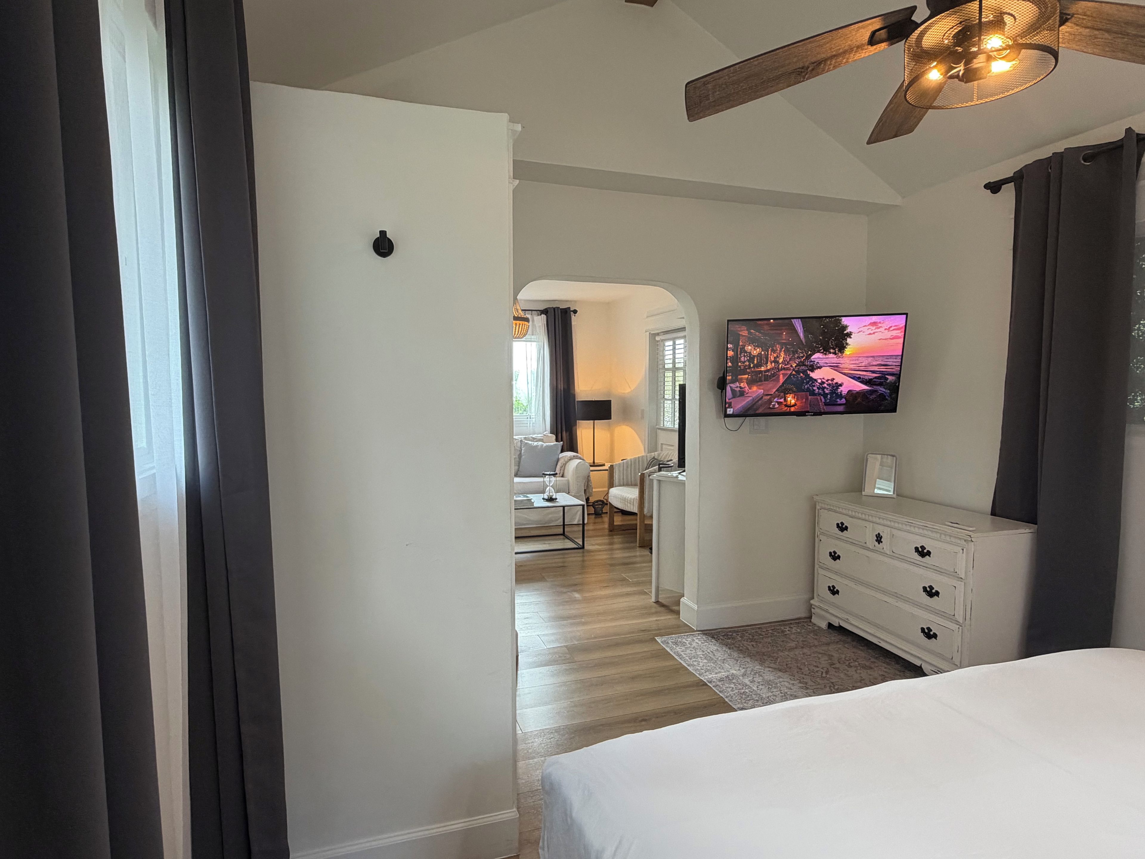 A hotel room with a bed, a TV on the wall, a dresser, and a ceiling fan.