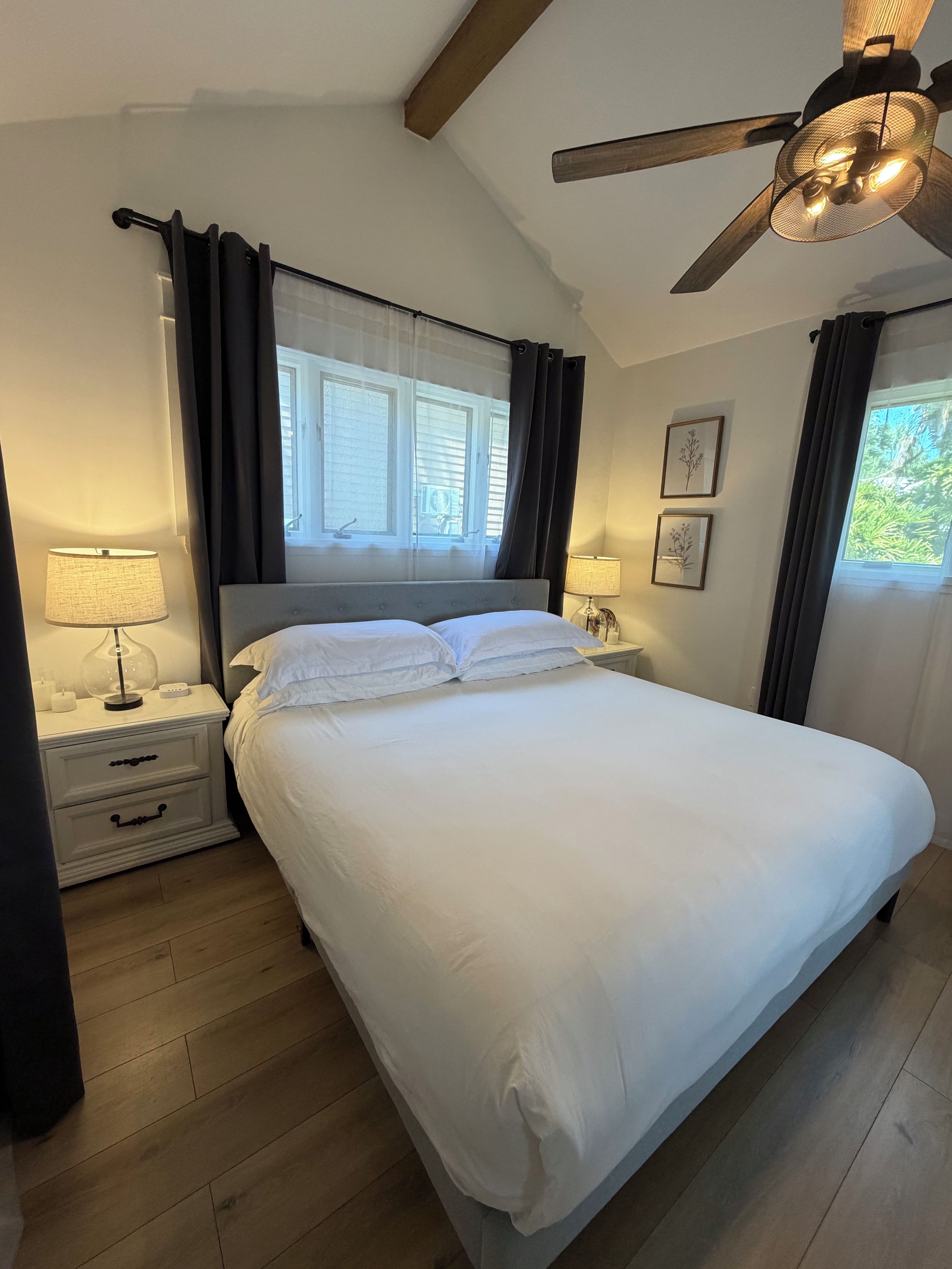 Una camera da letto con un letto, due comodini, una ventola a soffitto e una finestra con tende.