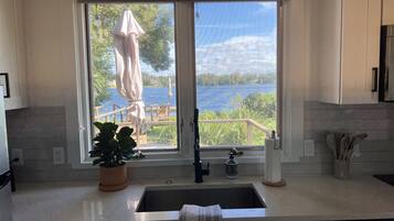 Una cocina con un amplio ventanal con vistas a un lago, una planta en maceta y una toalla colgada en la puerta.