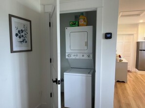 A compact laundry room with a washer and dryer, a small cabinet, and a digital clock on the wall.