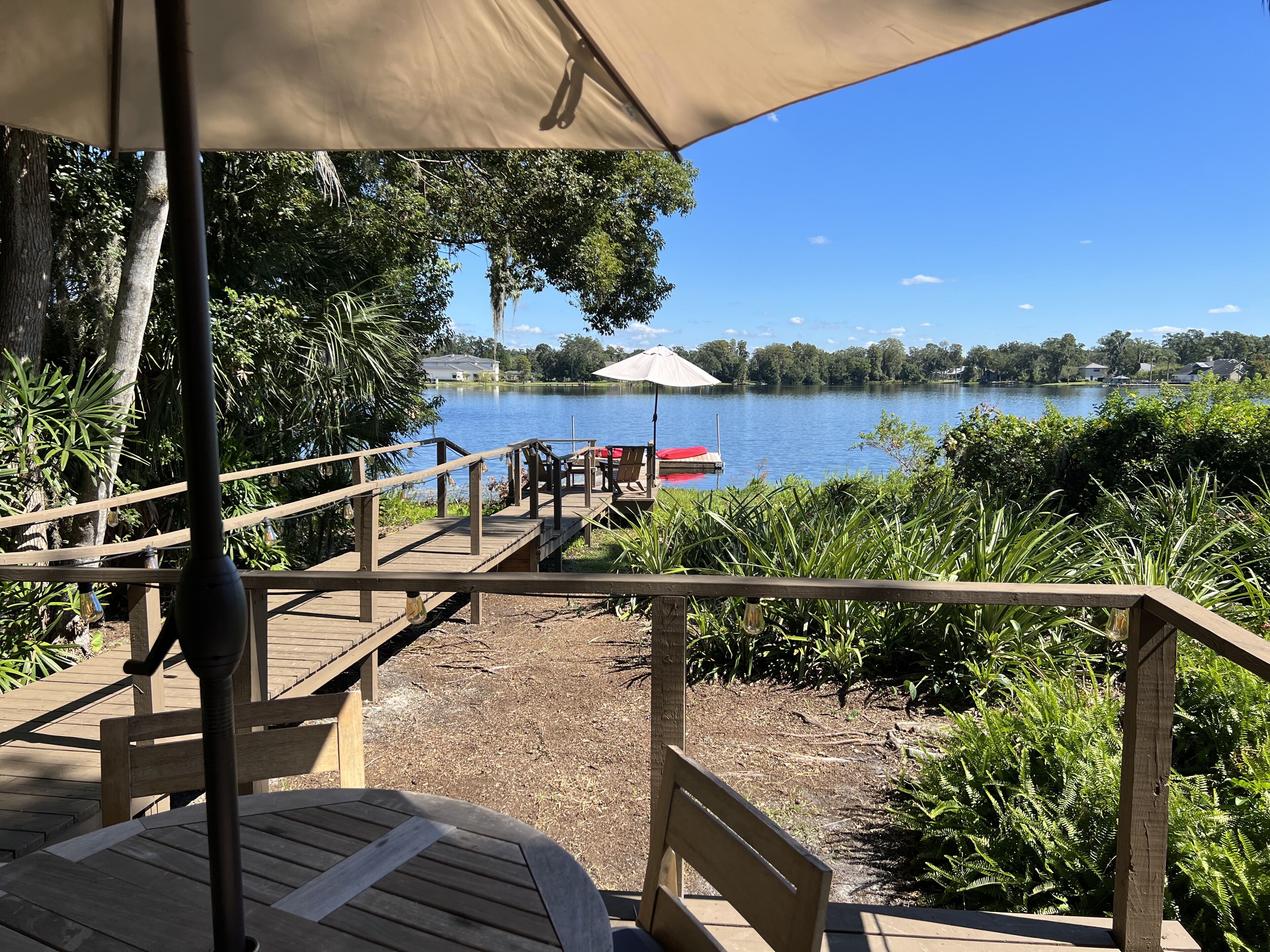 Una terraza de madera con una mesa y sillas, con vista a un lago que tiene un muelle y un bote.