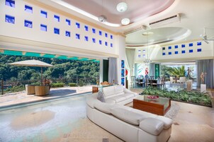 Amplia sala de estar con un sofá blanco grande, una mesa de centro de vidrio y vistas a un jardín exuberante.