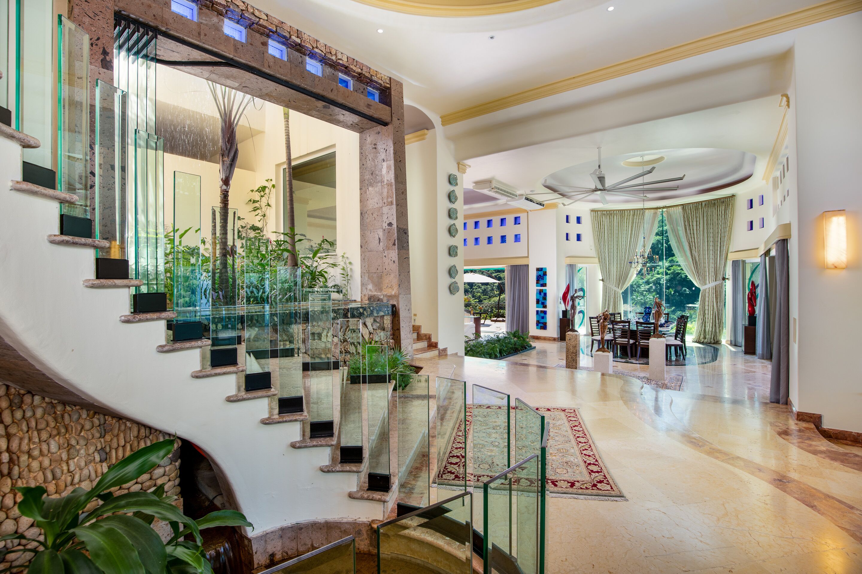 Un lobby imponente con una escalera de mármol, un ventilador de techo y un comedor con vistas al exterior.