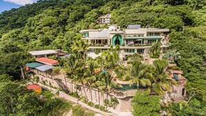 A multi-story resort with a pool surrounded by palm trees, set against a lush green hillside. - P V South Shore Luxury Accommodations (Puerto Vallarta)