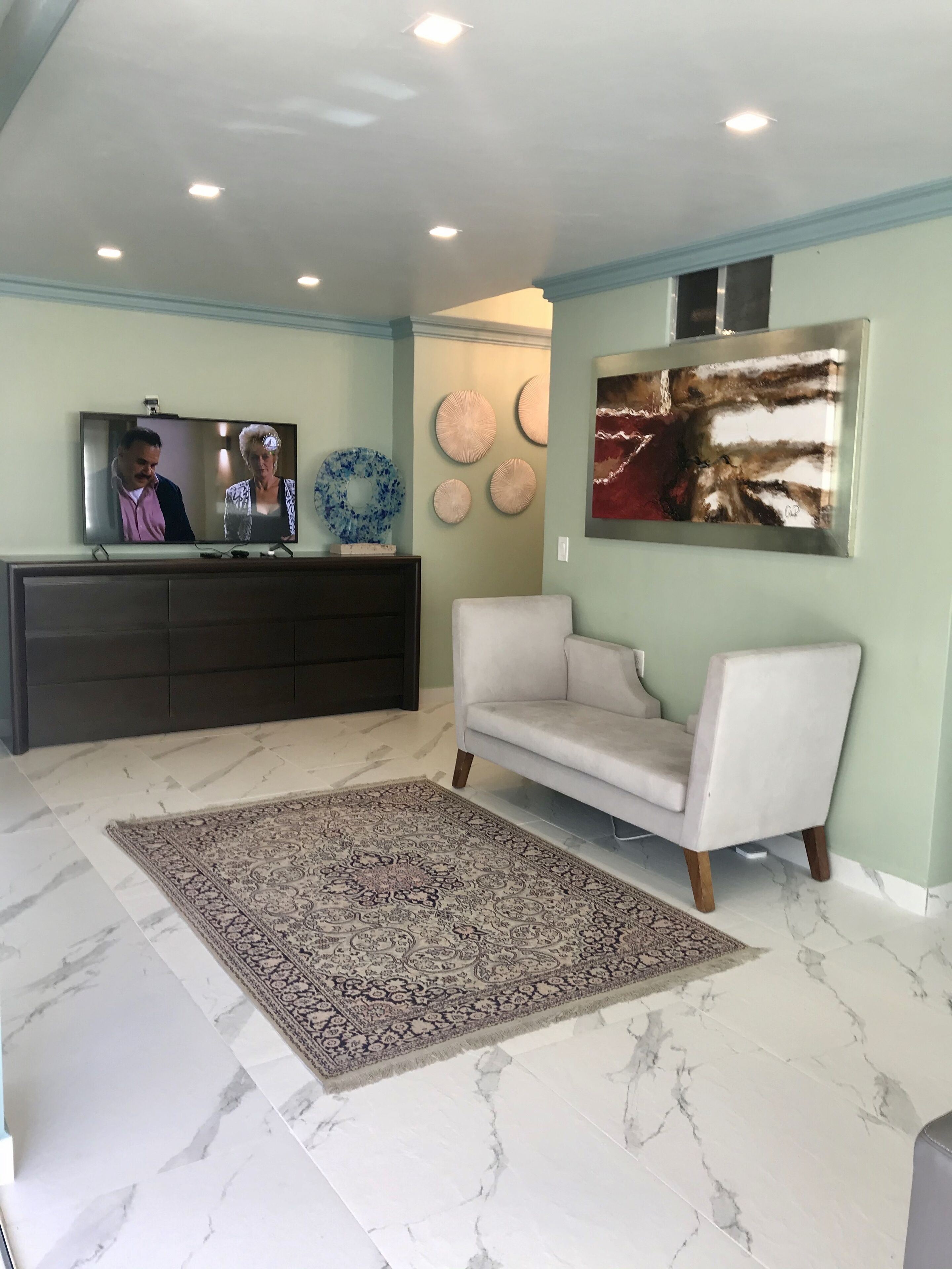 A living room with a television, a sofa, a patterned rug, and decorative wall art.