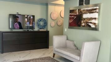 A living room with a television, a sofa, a patterned rug, and decorative wall art.