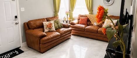 A living room with a brown leather sofa, a black entertainment unit, and a large orange vase with a plant.
