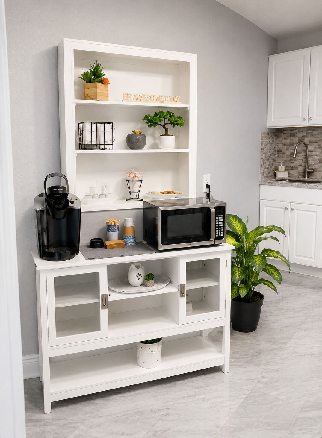 Une cuisine avec des meubles blancs, une machine à café, un four à micro-ondes et une plante en pot.