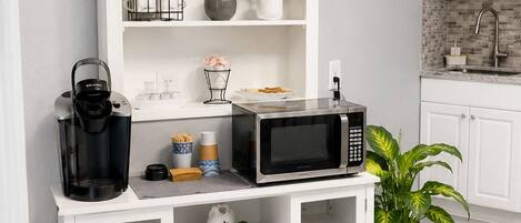 Une cuisine avec des meubles blancs, une machine à café, un four à micro-ondes et une plante en pot.