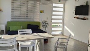 A modern living room with a sofa, a dining table with chairs, a TV mounted on the wall, and a ceiling fan. - Comfortable and safe apartment 3 minutes walk to the beaches (San Andrés y Providencia)
