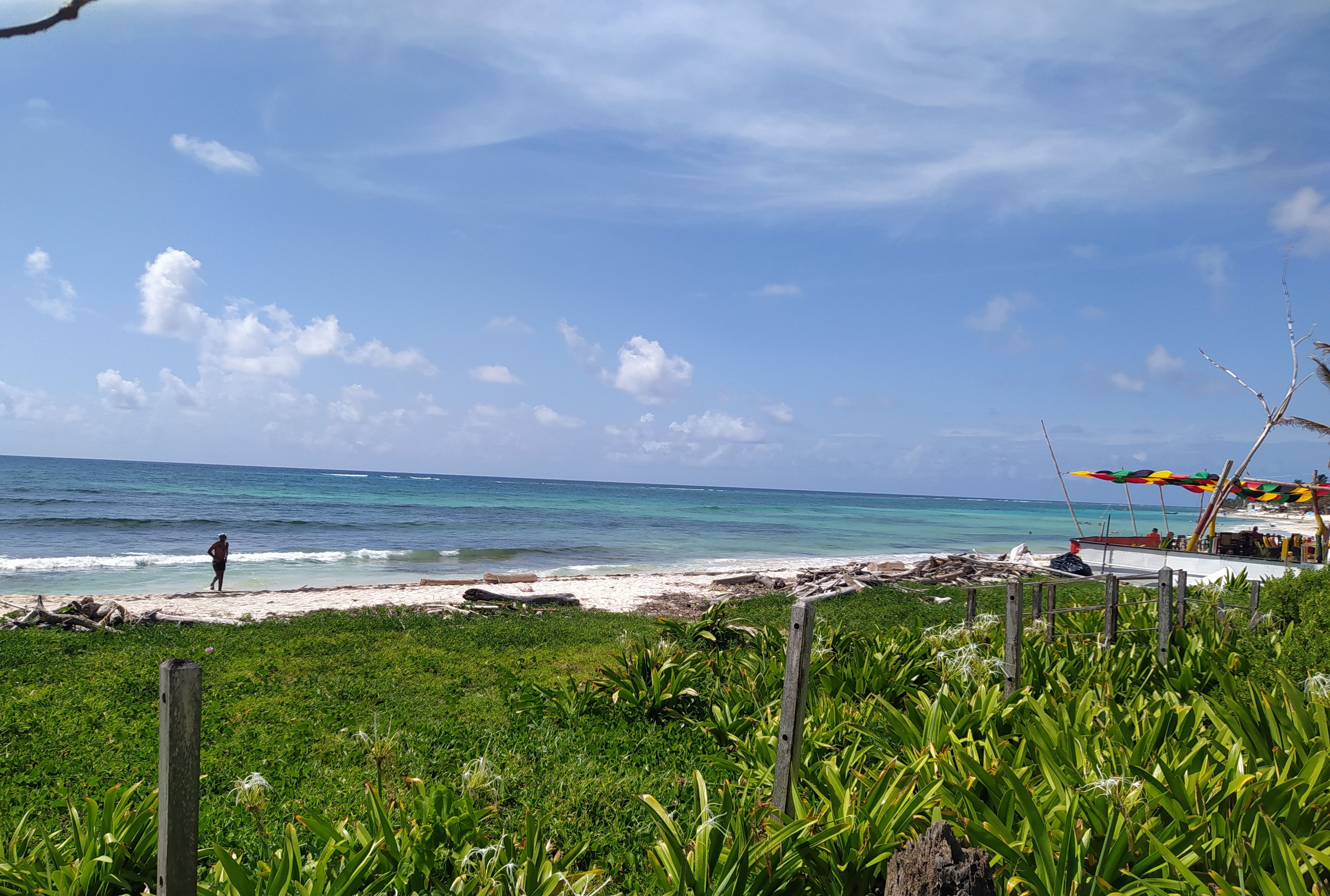 Una playa con una persona caminando, un bote y un paraguas colorido.