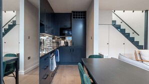Eine moderne Küche mit dunklen Schränken, ein Essbereich mit großem Tisch und Stühlen sowie eine Treppe, die zu einer oberen Ebene führt.