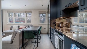 Eine moderne Küche mit Einbauofen, ein Essbereich mit Tisch und Stühlen sowie große Fenster, die für natürliches Licht sorgen.