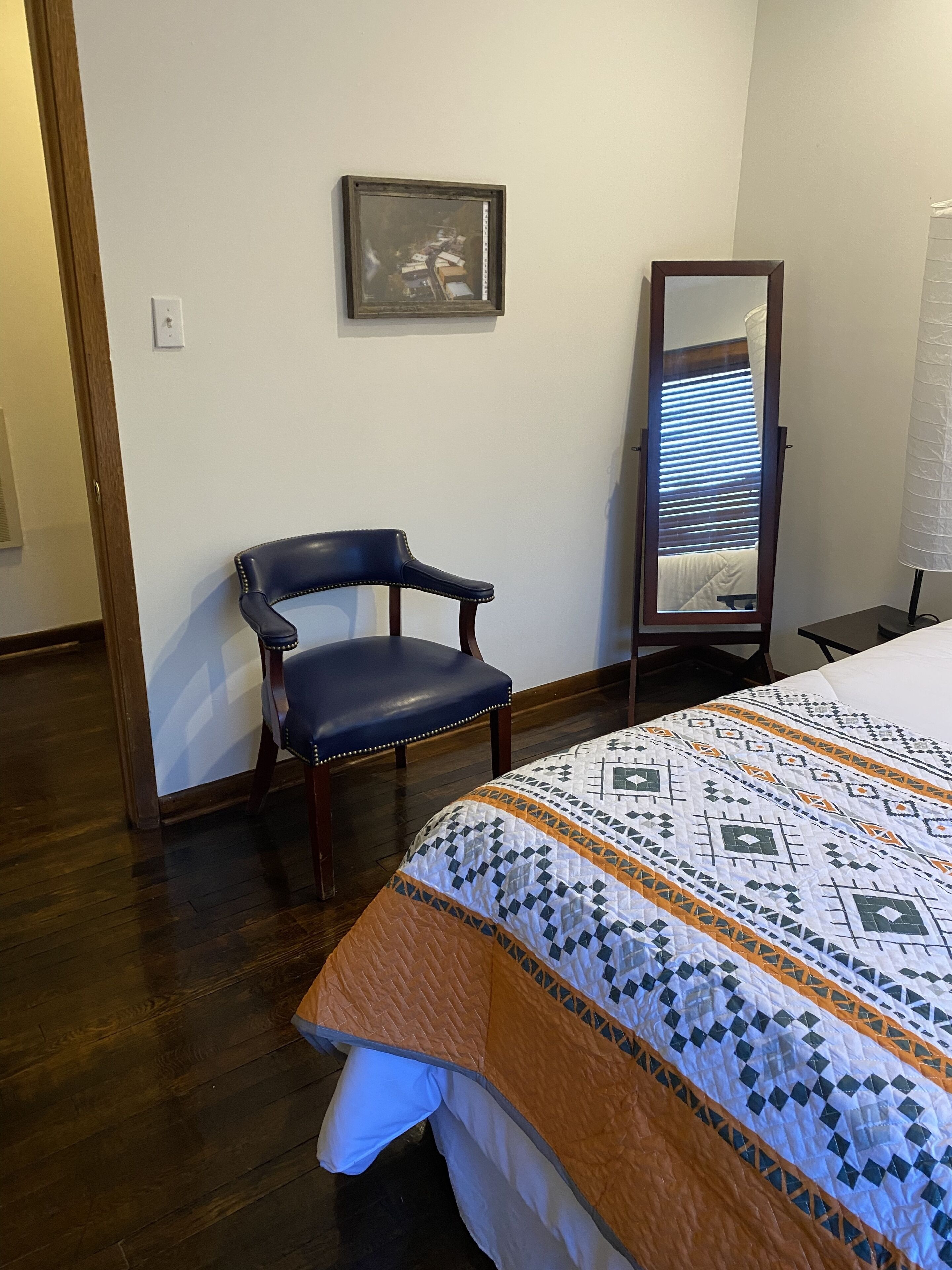 A bedroom with a bed, a chair, a mirror, and a wall-mounted picture.