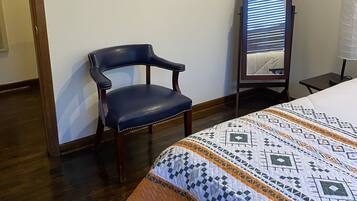 A bedroom with a bed, a chair, a mirror, and a wall-mounted picture.