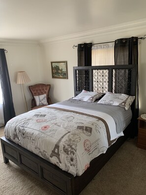 A bed with a Paris-themed bedspread, a wooden headboard, and a nightstand with a lamp. - The Chestnut Nest - Robinson (Robinson)