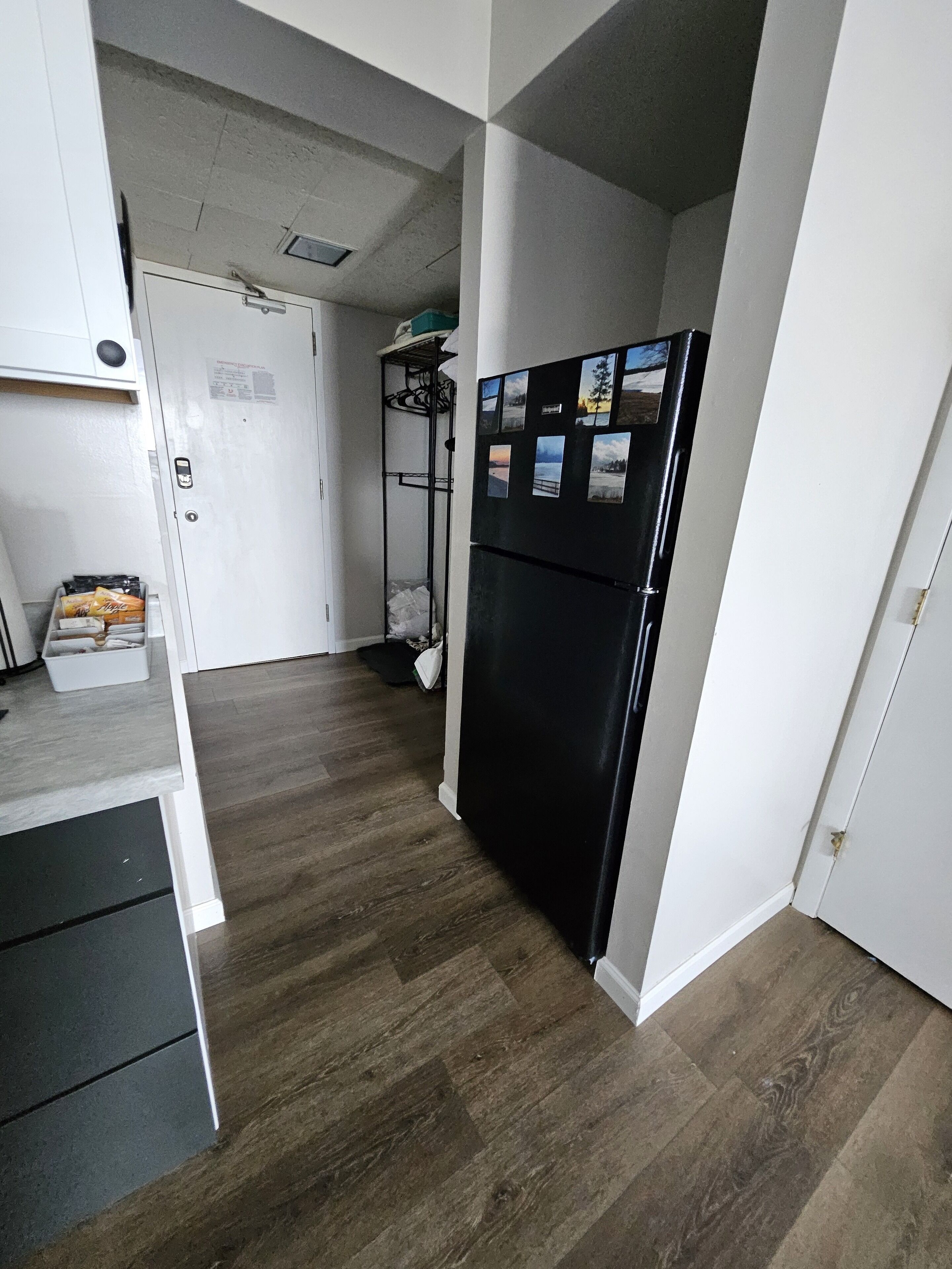 A compact kitchen with a black refrigerator, wooden flooring, and white walls.