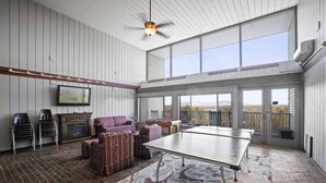 A spacious room with a ping pong table, a fireplace, and a large window overlooking a scenic view.