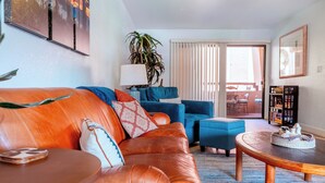 Un salón con un sofá de cuero marrón, un sillón azul, una mesa de centro de madera y una estantería.