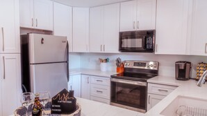Una cocina moderna con armarios blancos, electrodomésticos de acero inoxidable y una bandeja con una botella y vasos.