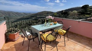A terrace with a table set for two, potted plants, and a view of the countryside. - Superba Vista by Interhome (Valloria)
