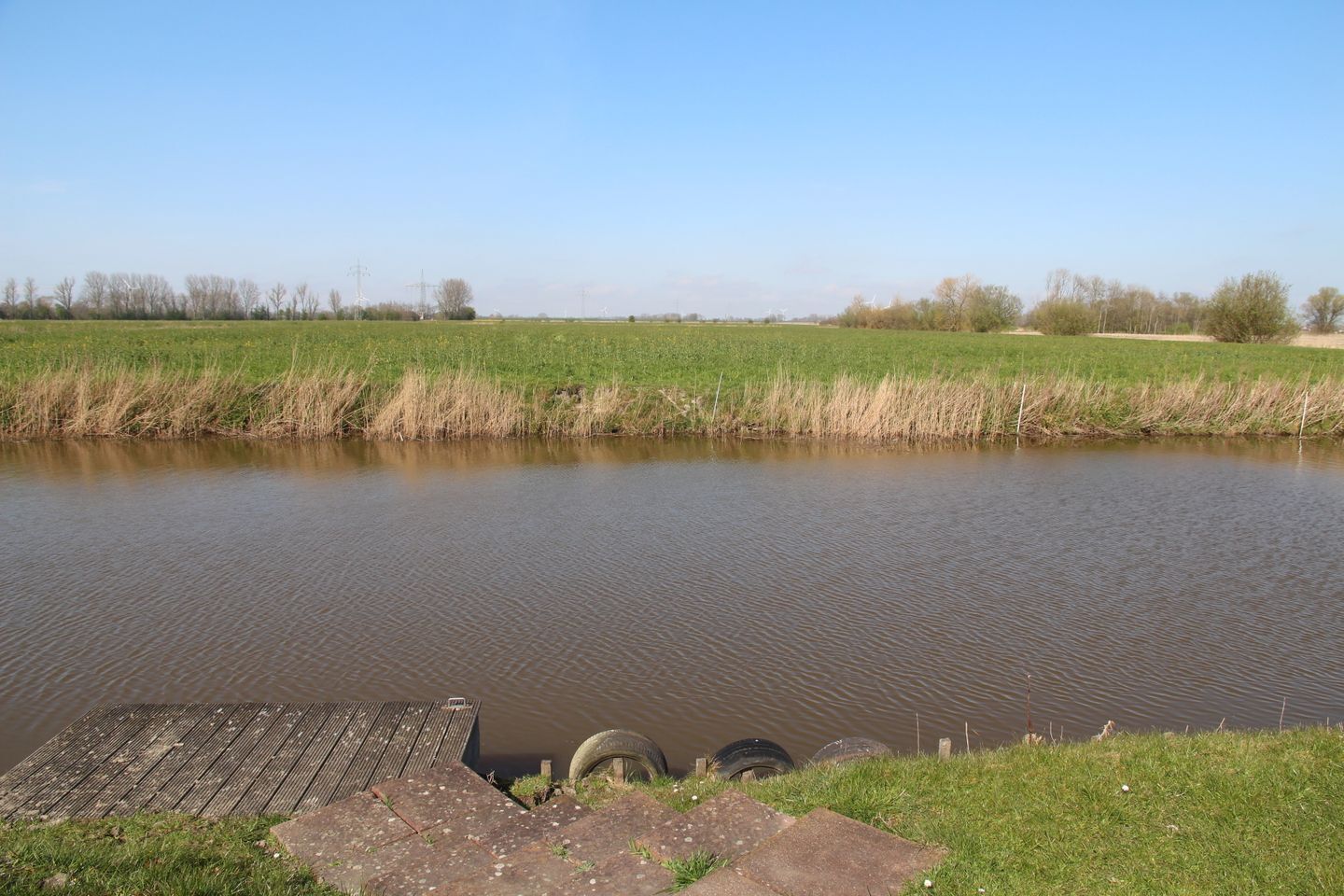 Een rustige rivier met een houten aanlegsteiger en banden op de oever.