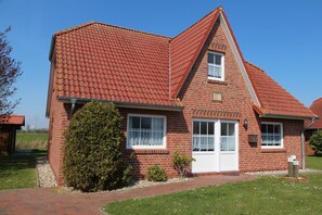 A two-story brick house with a red-tiled roof, white-framed windows, and a small front porch. - Wiesenblick Fenja - Wiesenblick Fenja Vacation Home: Sauna, Rowing Boat & Water View (Krummhörn)