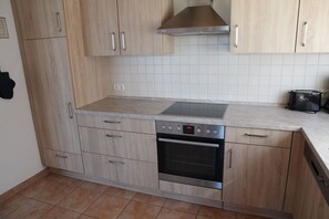 A modern kitchen with light wood cabinetry, a built-in oven, a stainless steel range hood, and a tiled backsplash. - Wiesenblick Fenja - Wiesenblick Fenja Vacation Home: Sauna, Rowing Boat & Water View (Krummhörn)