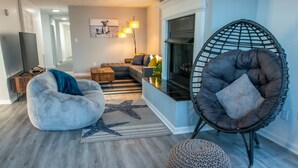 A modern living room with a sectional sofa, a bean bag chair, a round ottoman, and a unique chair with a mesh backrest. - Beachfront Getaway, Dolphin Suite, 🐶 💙 (Norfolk)