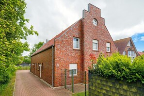 A red brick building with a gabled roof, a small circular window, and a number '22' on the side. - Leuchtfeuer - Beautiful vacation apartment (75sqm) for 4 persons and dog with balcony in (Krummhörn)