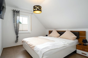 A bedroom with a bed, a nightstand, a lamp, a window with curtains, and a hanging light fixture.