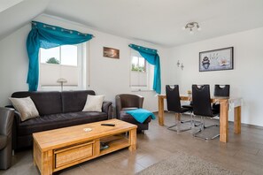 A living room with a sofa, coffee table, and a dining area with chairs and a table. - Leuchtfeuer - Beautiful vacation apartment (75sqm) for 4 persons and dog with balcony in (Krummhörn)