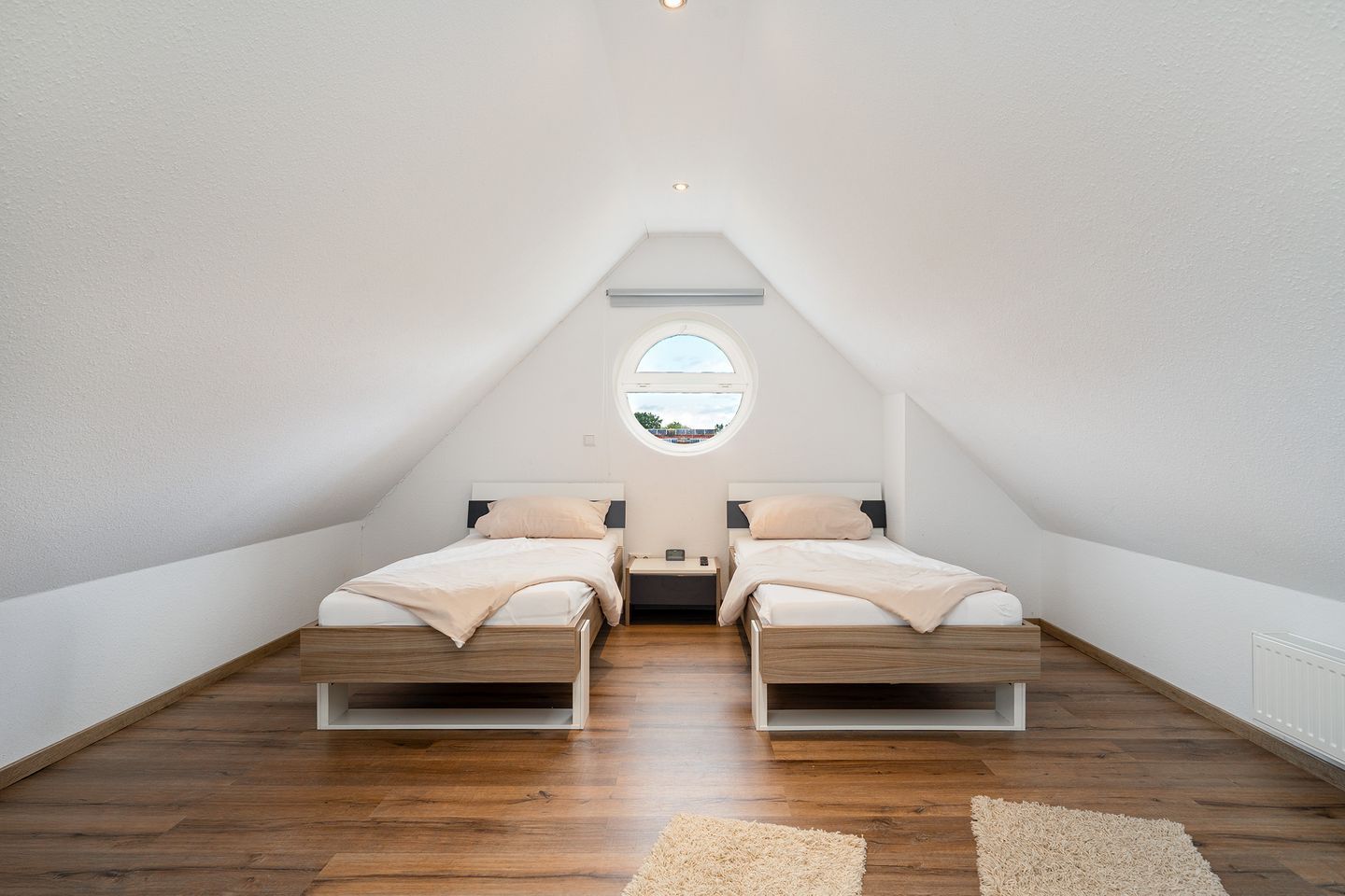A small, modern attic bedroom with two beds, a skylight, and wooden flooring.