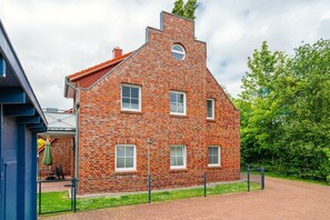 A red brick building with a gabled roof, multiple windows, and a small circular window on the second floor. - Leuchtfeuer - Leuchtfeuer Vacation Rental with a Balcony in Greetsiel (Krummhörn)