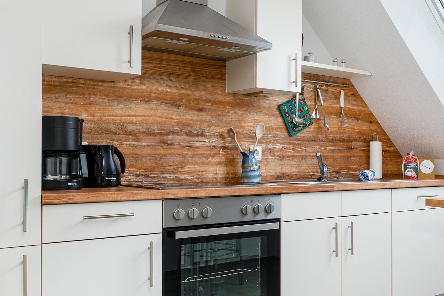 A modern kitchen with white cabinets, a wooden backsplash, and a stainless steel range hood.