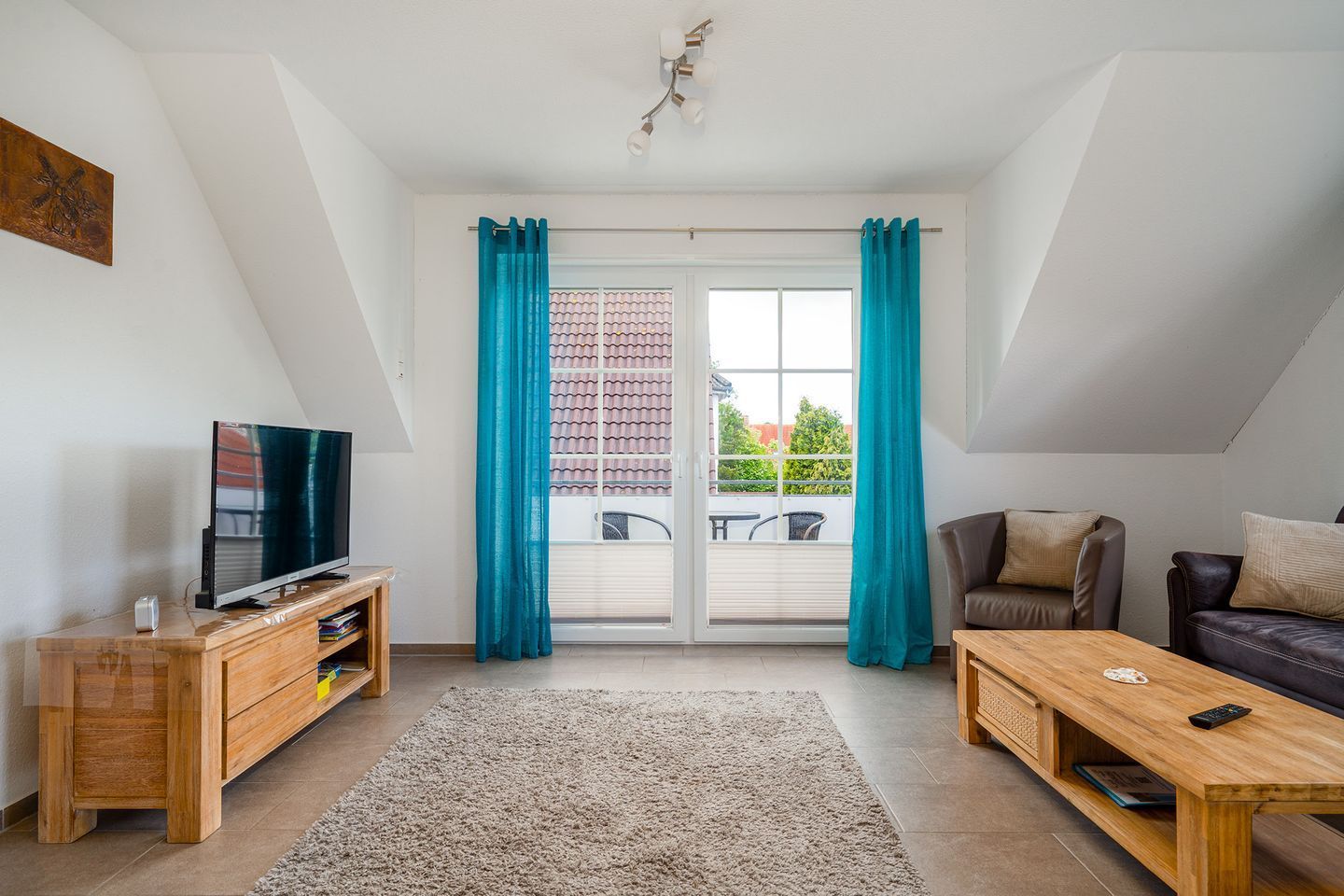 En moderne stue med fjernsyn, træmøbler, en sofa og udsigt til en balkon med blå gardiner.