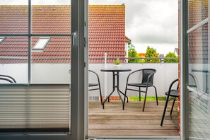 A balcony with a wooden floor, two black chairs, a small round table, and a potted plant. - Leuchtfeuer - Beautiful vacation apartment (75sqm) for 4 persons and dog with balcony in (Krummhörn)