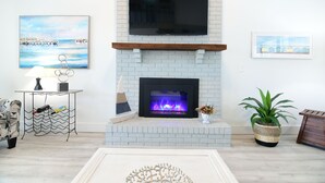 Ein modernes Wohnzimmer mit Kamin, einem Wand-Fernseher und Kunstwerken an den Wänden.