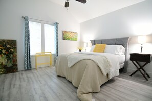 Une chambre à coucher avec un lit, une table de chevet, un ventilateur de plafond et une fenêtre avec des rideaux.