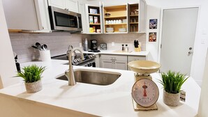 Eine moderne Küche mit weißen Schränken, einer Edelstahlspüle, einer Kaffeemaschine und zwei Blumentöpfen.