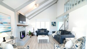 Ein geräumiges Wohnzimmer mit Kamin, zwei Sofas, einem Couchtisch und einem an der Wand befestigten Fernseher.