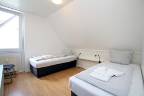 A bedroom with two beds, a radiator, a window, and a desk.