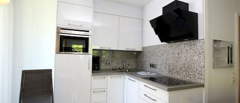 A modern kitchen with white cabinetry, a built-in oven, a coffee maker, and a granite countertop backsplash.