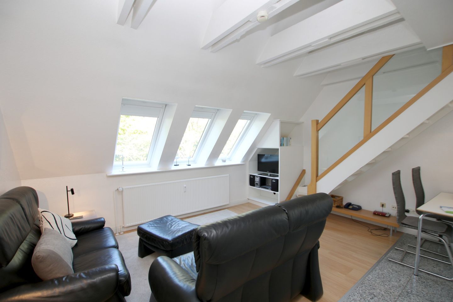 Ein modernes Loft-Apartment mit hohen Decken, Dachfenstern, einem eingebauten Fernseher, einer Couch, einem Esstisch und einer Treppe.