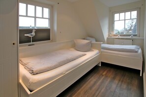 Een slaapkamer met twee enkele bedden, een radiator en een raam met een vogelvoerder.