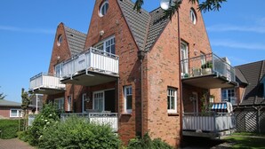 Een tweelaags bakstenen huis met een balkon op de tweede verdieping, een schotelantenne en een kleine tuin aan de voorzijde.